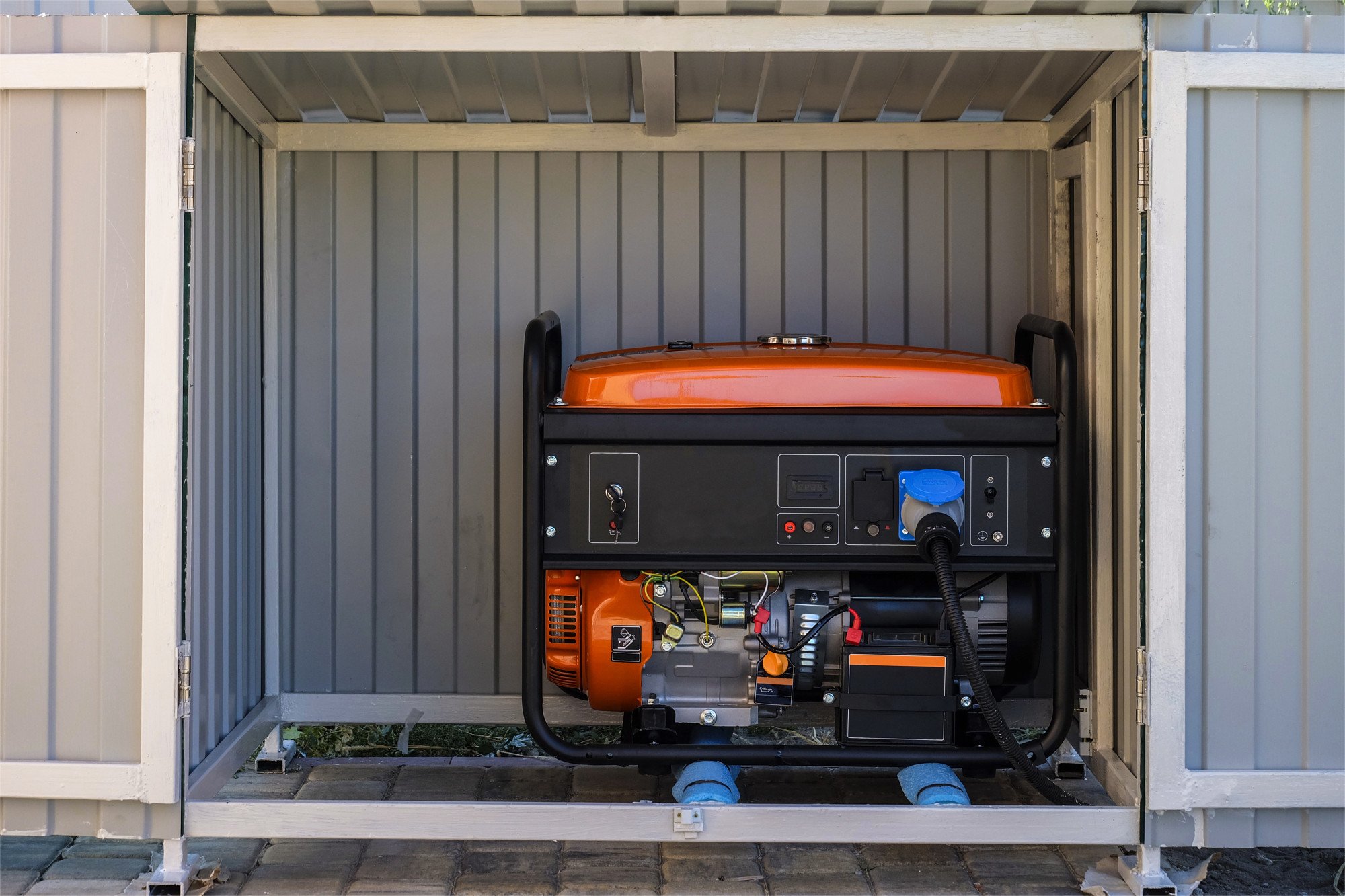Image of an orange, electrical generator tucked away in a grey shed.